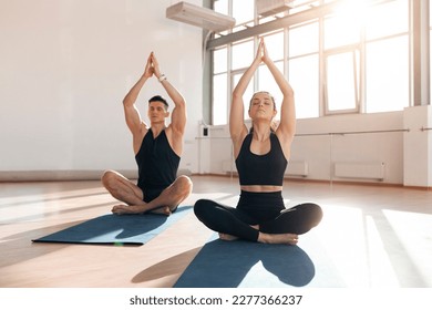 beautiful athletic couple in sportswear sit in yoga pose on yoga mats in the gym in the morning, fitness girl and trainer man meditate in light fitness room - Powered by Shutterstock