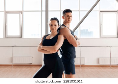 beautiful athletic couple in sportswear stands in the gym in morning, fitness girl and coach man stand back to back in training in bright room - Powered by Shutterstock