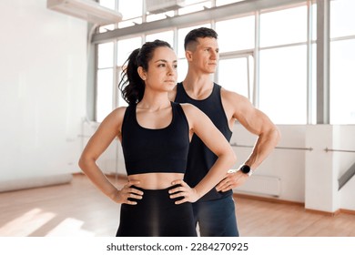 beautiful athletic couple in sportswear stands in the gym in the morning, fitness girl and coach man look to the side at the copy space at workout in bright room - Powered by Shutterstock