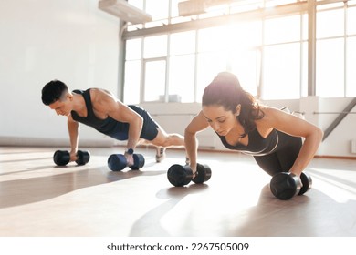 beautiful athletic couple in sportswear in training do push-ups with dumbbells in the fitness room in the morning, man trainer and fitness girl go in for sports in bright room - Powered by Shutterstock