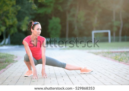 beautiful athletic female in sport bra stretching outdoors in sunny summer day, adult fit woman with perfect body at physical exercises in the fresh air before running