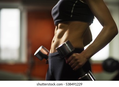 Beautiful athletic fitness woman  with abdominal  muscles. Part of fitness body. Sports and fitness - concept of healthy lifestyle. Young woman in the gym. Fitness girl with dumbbell