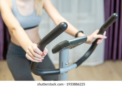 A beautiful athletic girl is engaged on an exercise bike in front of the window at home, front view, close-up. the concept of exercising or losing weight.