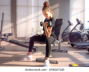 Beautiful athletic muscular woman pumps up the muscles by one arm lifts dumbbell exercise on bench in fitness gym. Young sport girl gains strong physical muscle well by weight lifted in fitness studio - Powered by Shutterstock