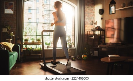 Beautiful Athletic Sports Woman Running on a Treadmill at Her Home Gym. Energetic Workout: Female Training while Listening Podcast or Music in Headphones. Apartment with Window View. Side Back View - Powered by Shutterstock