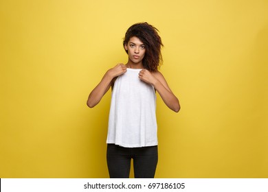Beautiful attractive African American woman posting and dressed up her white t-shirt. Yellow studio background. Copy Space.