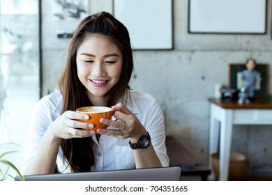 Beautiful Attractive Asian Business woman wearing white shirt smile and holding coffee in Coffee shop cafe with computer laptop on the table feeling so happiness and comfortable - Shutterstock ID 704351665