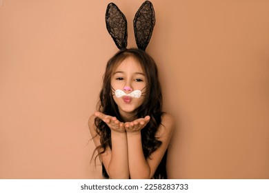 A beautiful attractive girl and ears decorated and face paints in rabbit  A child in the form an animal sends an air kiss  Easter Bunny