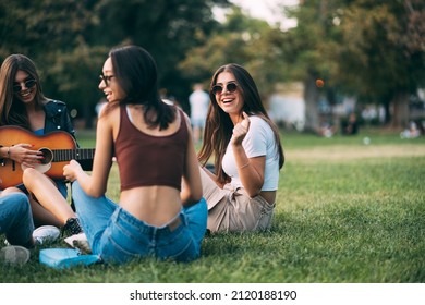 Beautiful and attractive girl friends are smiling and laughing while sitting on the grass