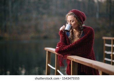 Beautiful Attractive Girl In A Red Hat On The Lake In Autumn Holds A Mug In Her Hands