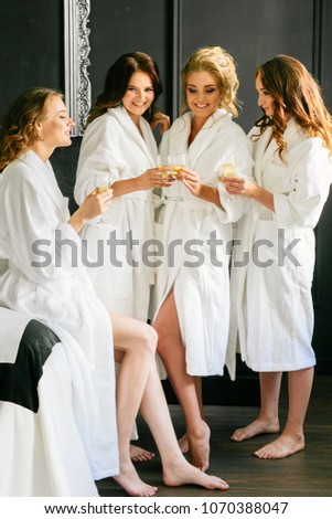 Beautiful attractive girls talking and drinking champagne in white coats on black wall background