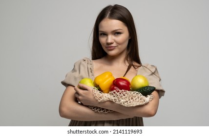 Beautiful attractive happy brunette woman holding mesh grocery bag with vegetables. Concept of no plastic. Zero waste, plastic free. Eco friendly concept. Sustainable lifestyle.