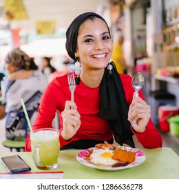 A Beautiful And Attractive Malay Muslim Woman In A Hijab Enjoys Nasi Lemak And Sugarcane Juice For Lunch During The Daytime In A Hawker Center In Singapore. 