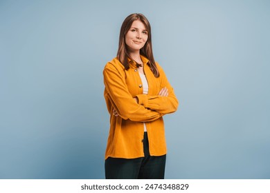 Beautiful, attractive, middle aged woman wearing casual yellow shirt with arms crossed standing isolated on blue background. Confident successful female looking at camera. Business concept