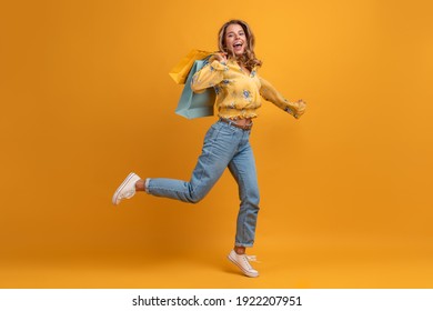 beautiful attractive smiling woman in yellow shirt and jeans jumping with shopping bags on yellow background isolated having fun emotional