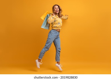 beautiful attractive smiling woman in yellow shirt and jeans jumping with shopping bags on yellow background isolated having fun emotional