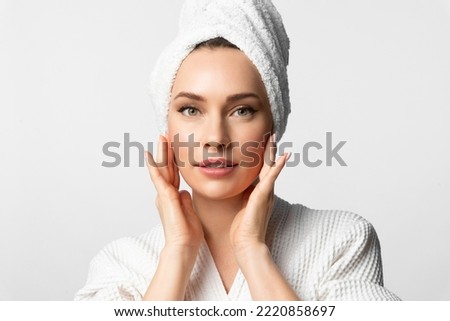 A beautiful attractive woman in bath clothes applies moisturizer cream to her face with her hands and smoothes her skin. The lady is taking care of herself.