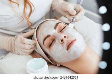 Beautiful and attractive young adult woman receiving professional beauty or skincare treatment with herbal clay mask. Modern and popular facial care treatment concept. Spa salon. High angle view. - Powered by Shutterstock