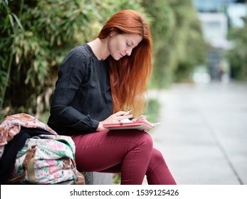 a beautiful attractive young red haired women sit in the park with bamboo in the background and read a book and enjoy her freetime with relaxing and reading