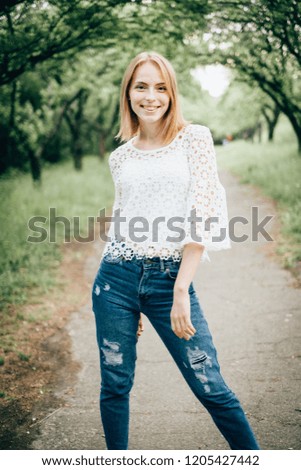Beautiful attractive young woman posing in spring park wearing white knitted top and blue jeans, modern creative toning