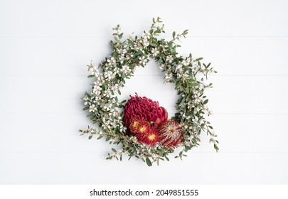 Beautiful Australian Native Flower Wreath, Photographed From Above, On A White Rustic Background. Mostly White Tea Tree Featuring A Red Waratah, Red Banksia Coccinea And Gum Nut Flowers.