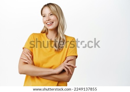Beautiful authentic blond girl, smiling woman cross arms on chest, posing in yellow t-shirt, standing over white background