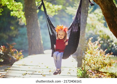 Beautiful autumn portrait of adorable preschooler girl in colorful maple leaves wreath on her head. Child having fun on garden swing or in hammock