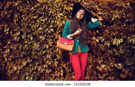 Beautiful Autumn Woman Holding Handbag Wearing Black Hat Against Leaves 