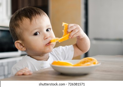 Beautiful Baby boy in the kitchen eagerly eating an orange, cut into wedges