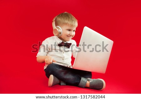 
beautiful baby boy sitting with a laptop in his hands and looking for information on the Internet on a red background. The concept of modern children and technology