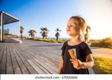 A Beautiful Baby Girl In A Black Dress On A Sunset With Ice Cream.