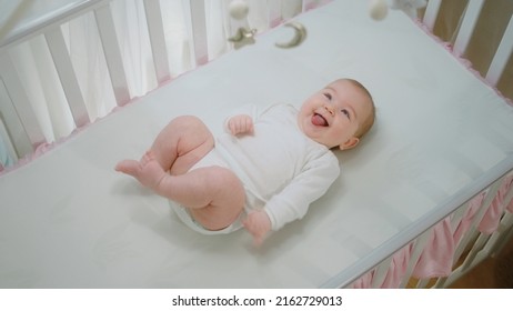 Beautiful Baby Girl Very Happy And Excited Smiling Large While Laying Down Alone In Her Baby Cot And Looking Up The Cot Toys