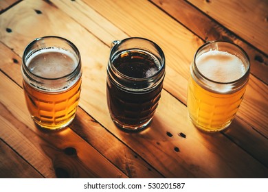 Beautiful Background Of The Oktoberfest. Glasses Of Cold Fresh White, Light And Dark Beer On The Wooden Bar Counter In The Pub. Assorted Alcohol In A Flight Ready For Tasting.