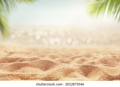 Beautiful background for summer vacation and travel. Golden sand of tropical beach, blurry palm leaves and bokeh highlights on water on sunny day.
