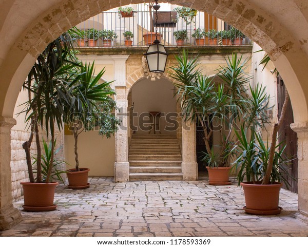 Beautiful backyard with arch, plants in pots,\
stairs and lantern. Patio decoration. Ancient courtyard background.\
Medieval architecture. Cozy italian backyard. Travel and\
architecture concept.