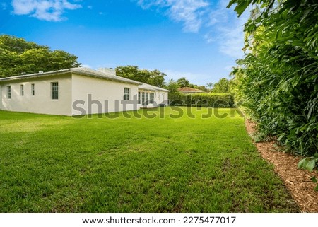 Beautiful backyard of modern and elegant house in the Golden Triangle neighborhood in the city of Coral Gables, short grass, tropical vegetation around, blue sky