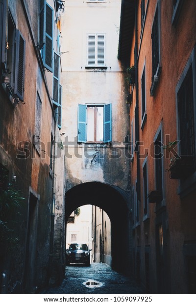 Beautiful backyard, narrow\
street and vintage old windows in Rome, Italy. Sunny day, shadows,\
amazing quite atmosphere of Trastevere district. Lone parked\
car.