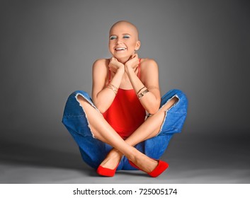 Beautiful Bald Woman Sitting Against Grey Background