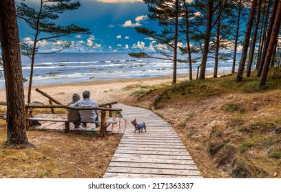 Beautiful Baltic Coastal Landscape And Couple Of Seniors With A Small Dog Are Resting On Sandy Beach Of The Baltic Sea In Jurmala - Famous Tourist Resort In Latvia