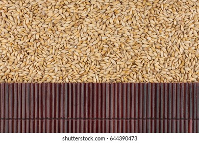 Beautiful bamboo mat on barley grains as agricultural background. View from above