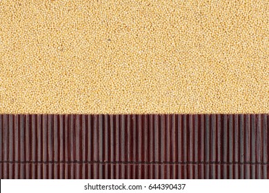 Beautiful bamboo mat on millet grains as agricultural background. View from above
