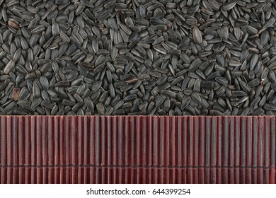 Beautiful bamboo mat on sunflower seeds as agricultural background. View from above