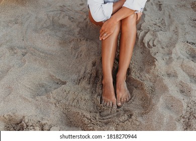 Beautiful Bare Legs Of A Girl. A Girl Sits On The Sand.