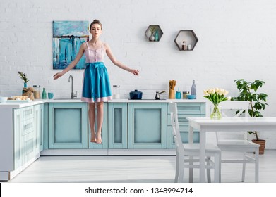 Beautiful Barefoot Girl In Apron Levitating In Air In Kitchen