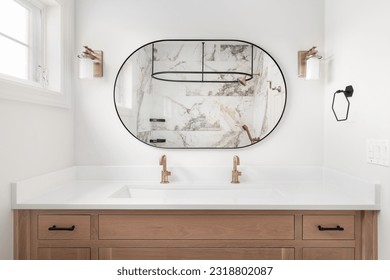 A beautiful bathroom with a white oak cabinet, marble countertop, gold faucets and lights, and a marble shower through a round mirror. - Powered by Shutterstock