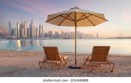 Beautiful Beach In Dubai With 2 Sun Chairs And An Umbrella. In The Background Is The Skyline Of Dubai Marina