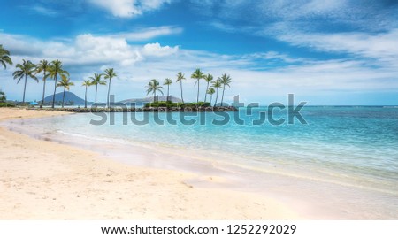 A beautiful beach scene in the Kahala area of Honolulu, with fine white sand, shallow turquoise water, a view of coconut palm trees and Koko Head in the background.