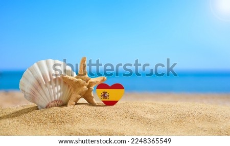 Beautiful beach in Spain. Flag of Spain in the shape of a heart and shells on a sandy beach.