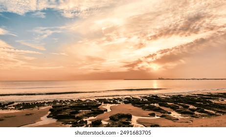 Beautiful beach at sunset with a vibrant sky in orange and blue hues. Gentle waves meet the rocky shore, reflecting the warm colors of the setting sun. Ideal for travel and nature-themed projects. - Powered by Shutterstock