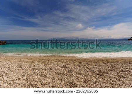 A beautiful beach where instead of sand there are small round pebbles overlooking the turquoise sea.